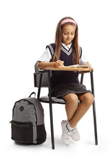 Beautiful schoolgirl sitting in a school chair and writing homework