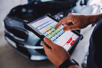Mechanic using tablet for diagnosing a car issue. Garage of car salon interior.