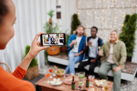 Young woman taking smartphone photo of diverse group of young people during outdoor party at rooftop