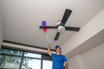 Man on ladder cleaning the blades of a ceiling fan