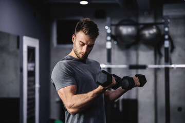 Fototapeta na wymiar The smoldering look of an attractive and muscular man. A man in sportswear pumps his arm muscles and lifts dumbbells in a modern gym. Close up shot of a male person