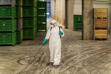 Person in a white protective suit refreshing and cleaning a hallway of warehouse indoor space Fight...