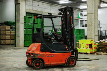 Fototapeta na wymiar In focus forklift in the warehouse. The old rusty forklift is in an empty warehouse with no people. In the background are boxes and pallets for packing fresh fruits and vegetables. Transportation