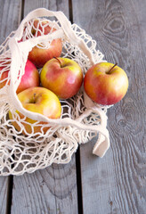 Red-yellow ripe juicy apples in a handmade mesh on a wooden background. Environmental concept. Side view. selective focus