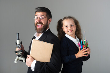 Amazed teacher with excited happy pupil school girl. Portrait of funny school girl and tutor with school supplies. Happy teacher and student girl on gray. Back to school, student girl in uniform.