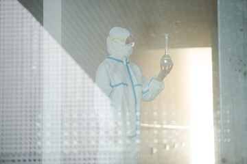 Fototapeta premium Scientist in clean suit examining liquid in test tube