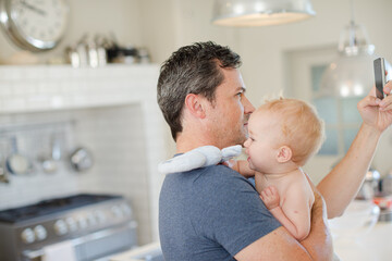 Fototapeta premium Father holding baby and checking cell phone