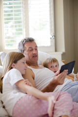 Obraz premium Father and children using digital tablet on bed