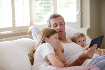 Obraz premium Father and children using digital tablet on bed