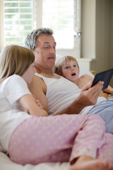 Obraz premium Father and children using digital tablet on bed