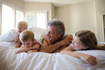 Obraz premium Father and children relaxing on bed