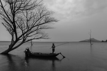 fisherman on wooden boat casting a net for catching freshwater fish in nature river in the early...