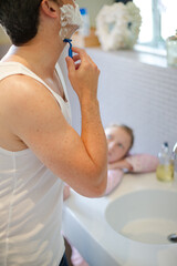 Girl watching father shave in bathroom