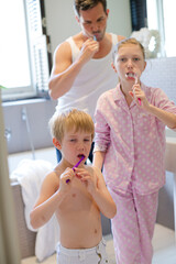 Father and children brushing teeth in bathroom