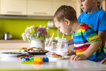 Funny male brothers eat cookies with round multi-colored sweets m&m and drink milk.