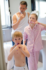 Father and children brushing teeth in bathroom