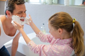 Obraz na płótnie Canvas Girl rubbing shaving cream on father's face