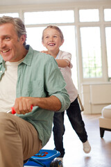 Boy pushing father on tricycle indoors