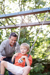 Father pushing son on swing outdoors