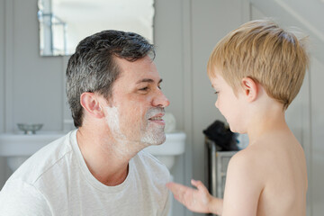 Boy rubbing shaving cream on father's face