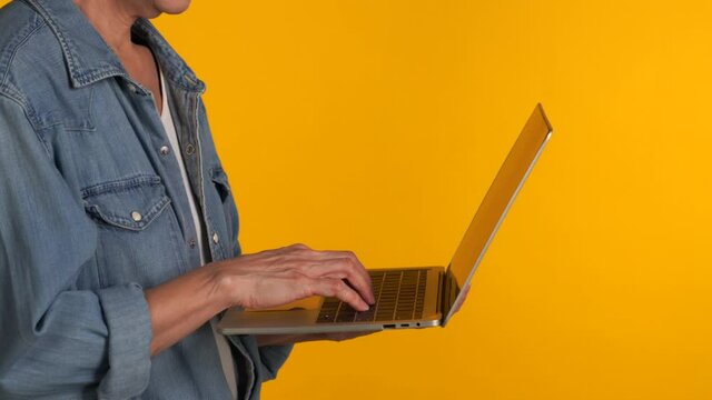 Middle aged Asian woman using laptop isolated on yellow background