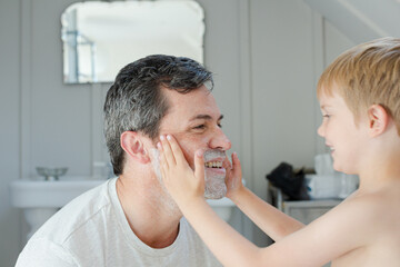 Boy rubbing shaving cream on father's face
