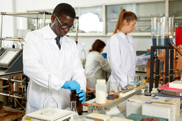 Focused man lab technician in glasses working with reagents and test tubes, woman on background