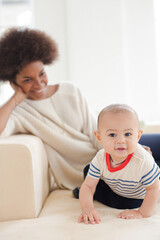 Mother watching baby boy crawl in living room