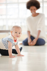 Mother watching baby boy crawl in living room