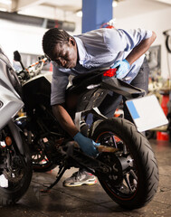 Fototapeta na wymiar Afro american man working at restoring motorbike in motorcycle workshop. High quality photo