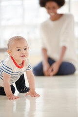 Mother watching baby boy crawl in living room