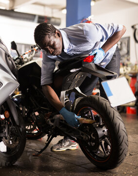 Afro american man working at restoring motorbike in motorcycle workshop. High quality photo