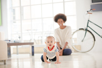 Fototapeta premium Mother watching baby boy crawl on floor