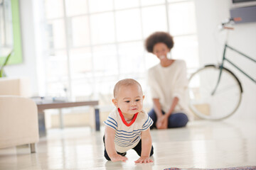 Mother watching baby boy crawl on floor