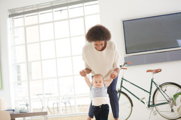Fototapeta na wymiar Mother helping baby boy walk in living room