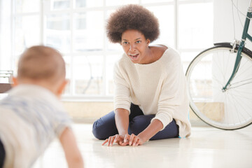 Mother watching baby boy crawl on floor