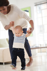 Mother helping baby boy walk in living room