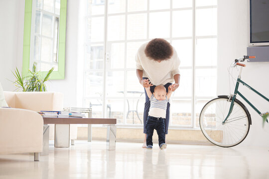 Mother helping baby boy walk in living room