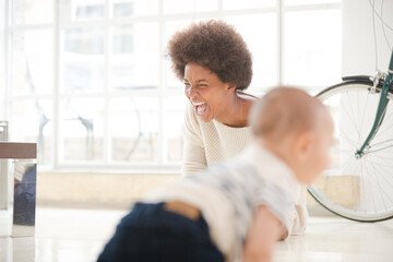 Mother watching baby boy crawl on floor