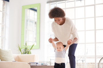 Fototapeta na wymiar Mother helping baby boy walk in living room