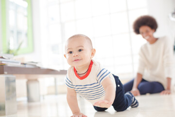 Mother watching baby boy crawl on floor