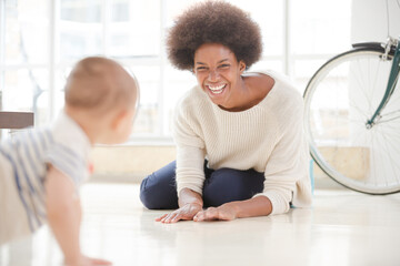 Mother watching baby boy crawl on floor