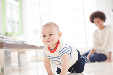 Mother watching baby boy crawl on floor