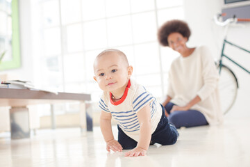 Mother watching baby boy crawl on floor