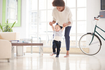 Mother helping baby boy walk in living room