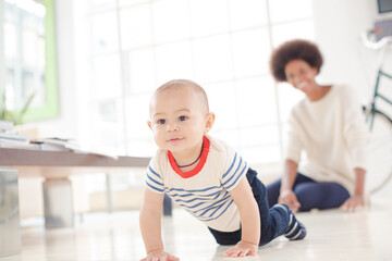 Mother watching baby boy crawl on floor