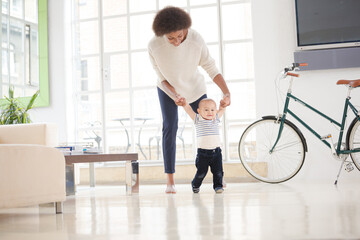 Mother helping baby boy walk on floor