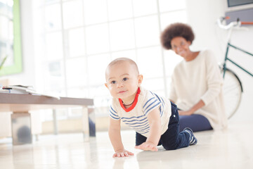 Mother watching baby boy crawl on floor