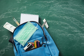 Fototapeta na wymiar Top view of stylish blue school bag backpack at a green chalkboard with face mask protection and stationery, Back to school education new normal during outbreak COVID-19 or coronavirus concept