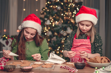 Happy girlfriends showing decorated gingerbread at home